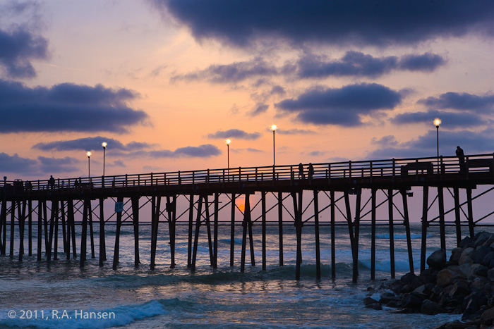 A few hardy pedestrians stoll along the pier as the sun sets behind the clouds