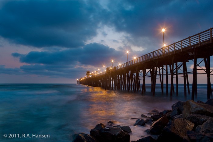 The sun has set under a cloudy sky and the pier lights have come on, glowing with their reflection in the water below