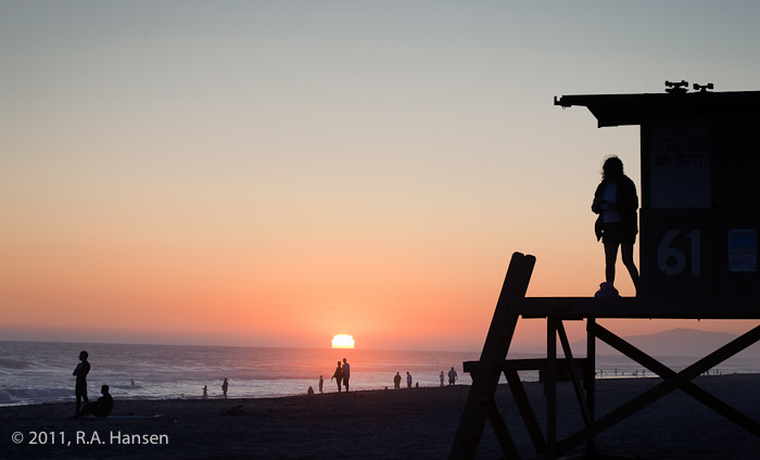 Sunset over the beach with a lifeguard station in the foreground and the Palos Verdes Peninsula in the background.