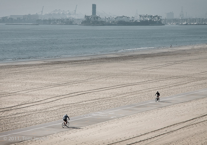 A cold winter morning on the beach with two lone bicyclists and the Port of Long Beach in the background. Photo by Tom Jewett