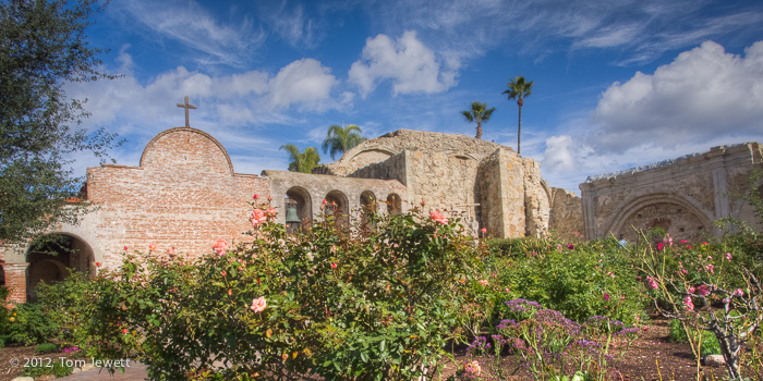 View of the entrance garden and south side of the mission, with dramatic clouds above. Included are the mission bells in the...